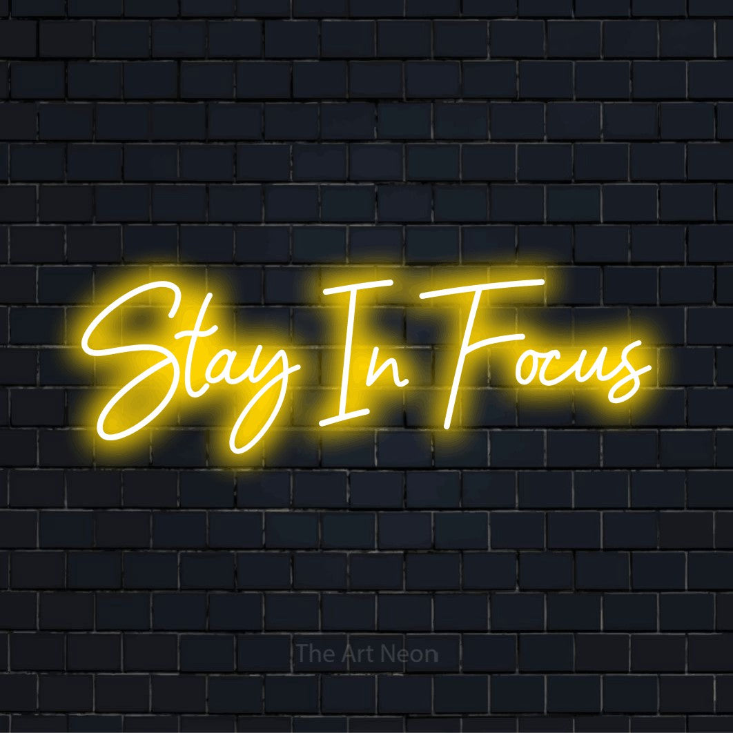 "Stay In Focus" glowing LED neon sign on a black brick wall