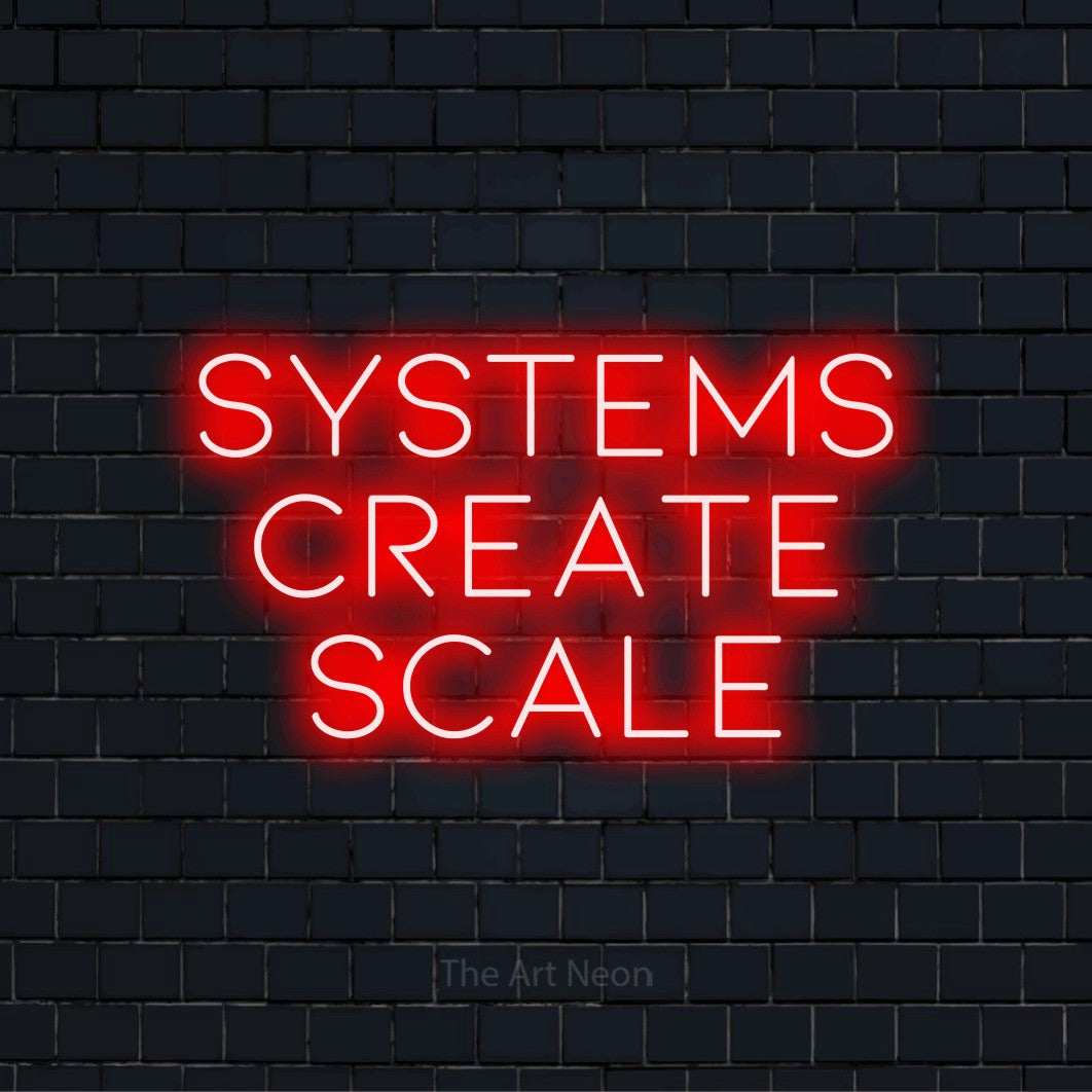"Systems Create Scale" script-style LED neon sign on a black brick wall