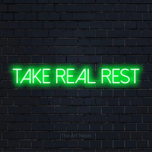 "Take Real Rest" script-style LED neon sign on a black brick wall