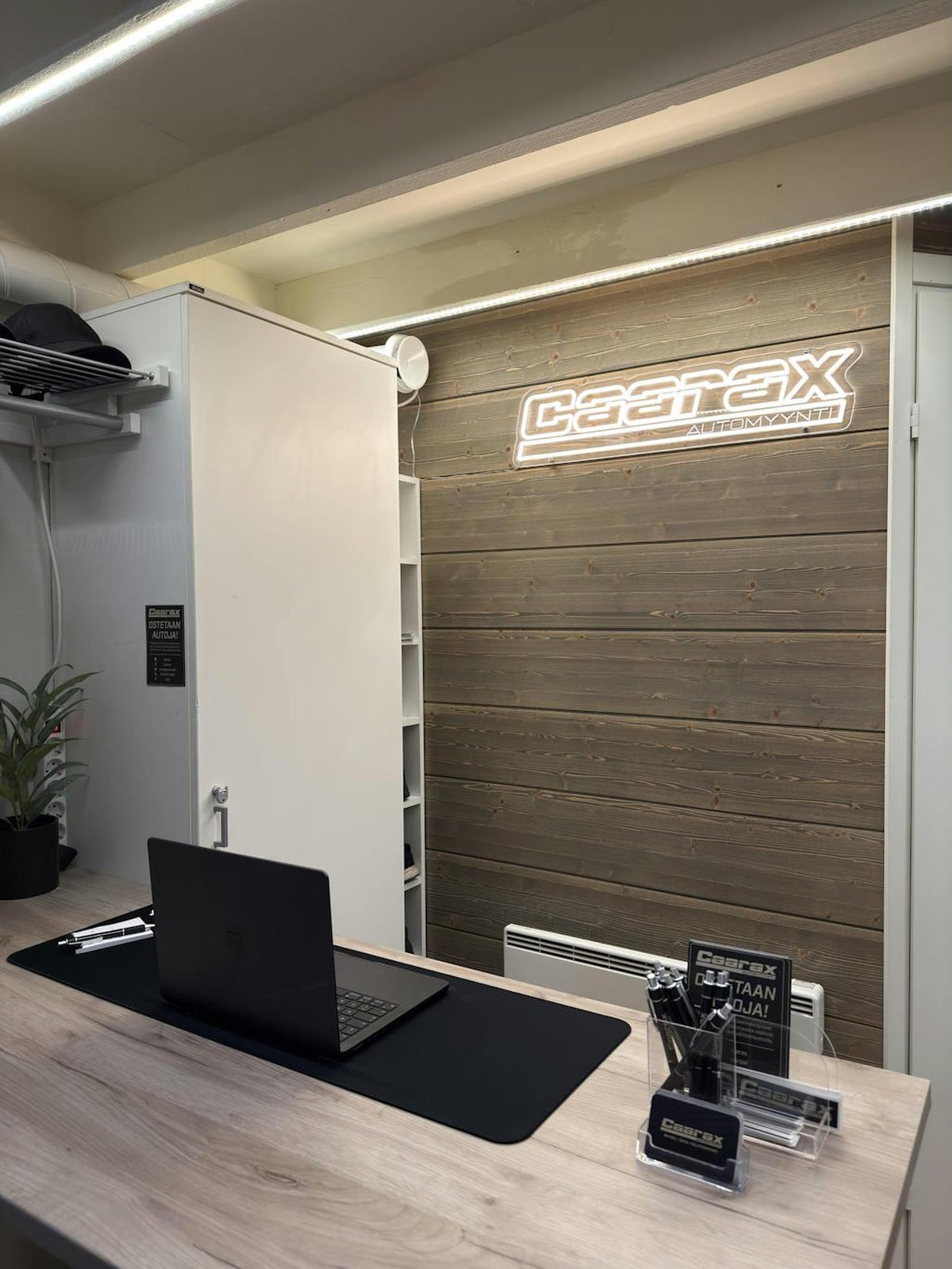 Warm-white Caarax Automyynti logo LED neon installed on a wood-panel office wall.