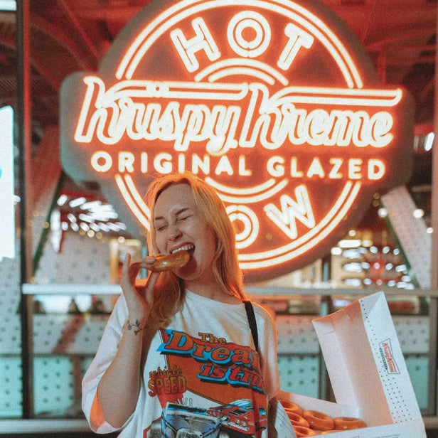 Person eating a doughnut in front of a Krispy Kreme sign