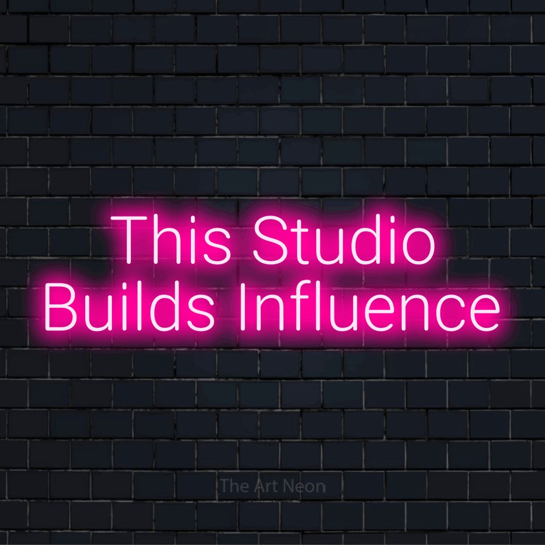 "This Studio Builds Influence" script-style LED neon sign on a black brick wall