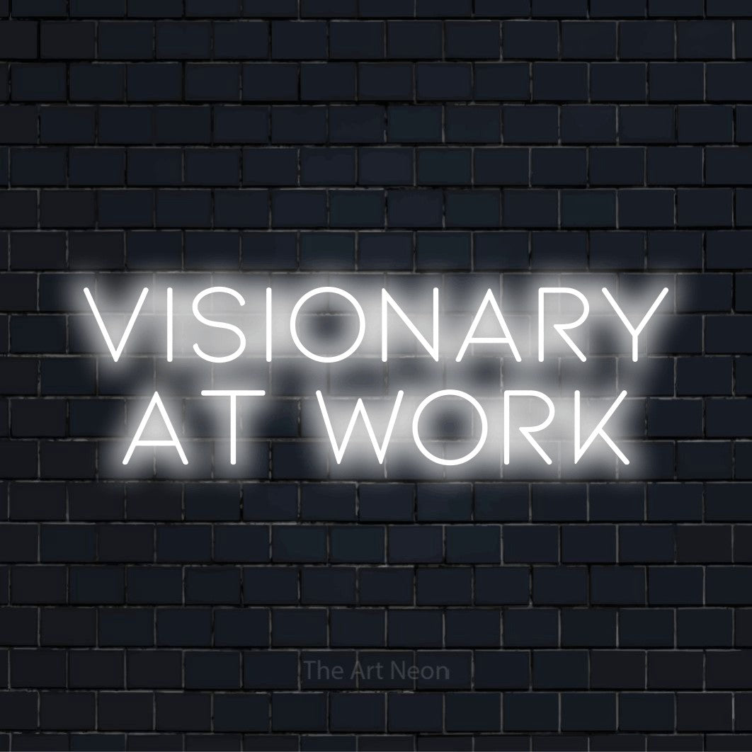 "Visionary At Work" glowing LED neon sign on a black brick wall