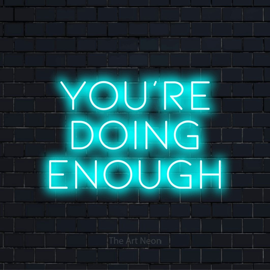"You’re Doing Enough" text design with neon effect on a black brick wall