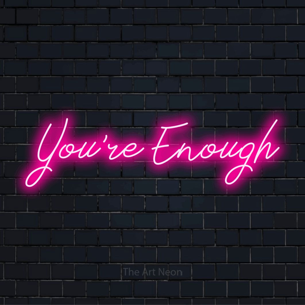 "You’re Enough" script-style LED neon sign on a black brick wall
